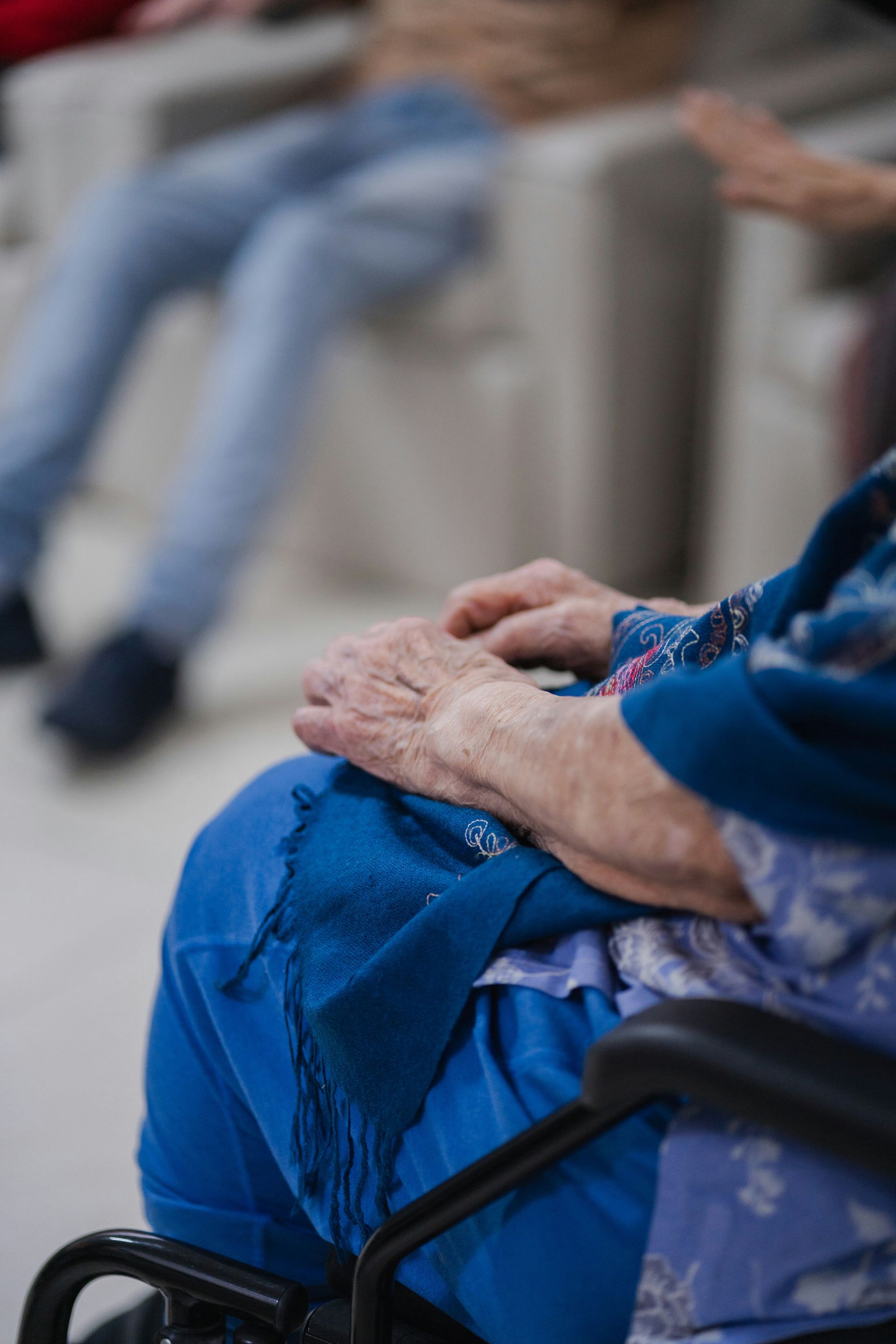Elderly hands resting on a blue lap in a wheelchair